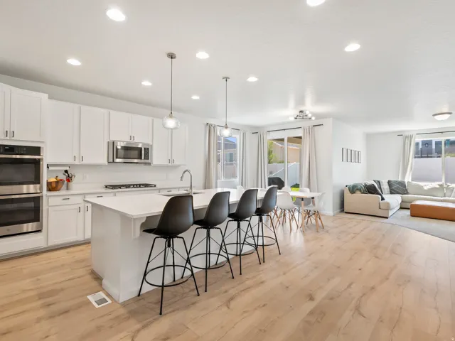 Spacious open concept living area featuring a kitchen with white cabinetry, stainless steel appliances, and a large island with seating