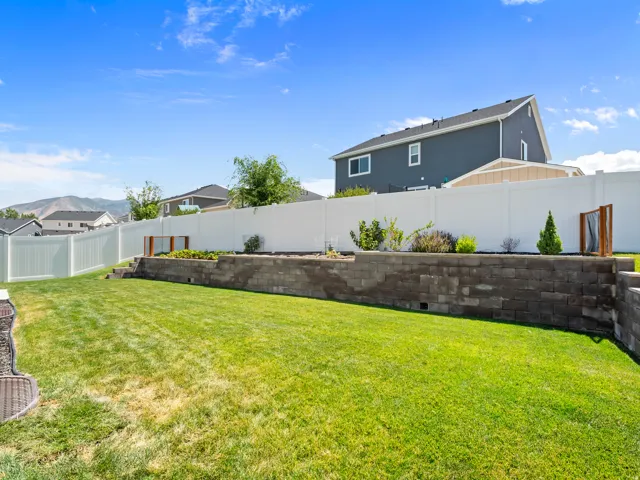Expansive backyard featuring a large green lawn, tiered landscaping with a retaining wall, and full vinyl fencing