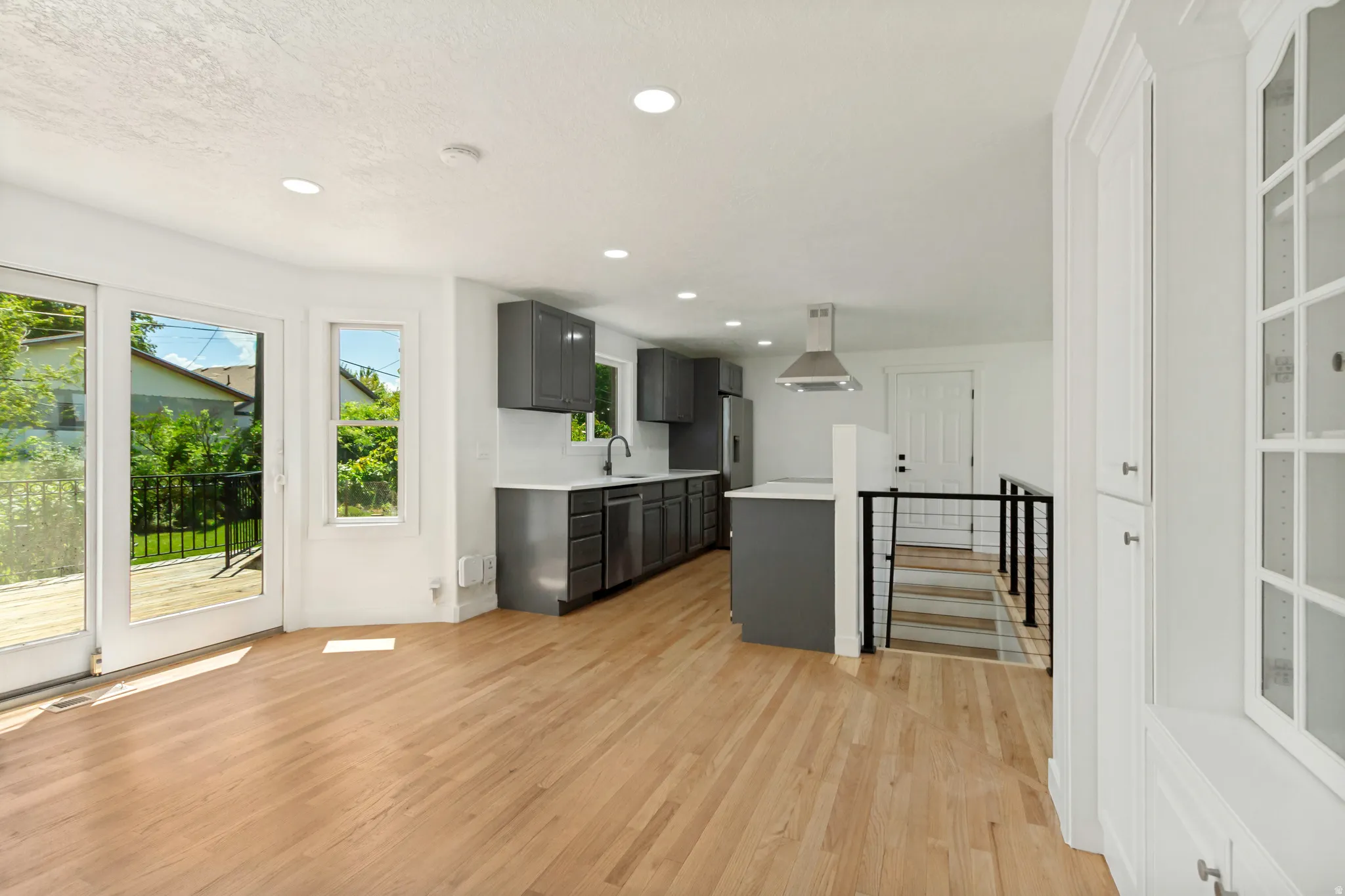 Open-concept living space featuring wood-finish flooring, recessed lighting, and a modern kitchen with gray cabinetry and stainless steel appliances