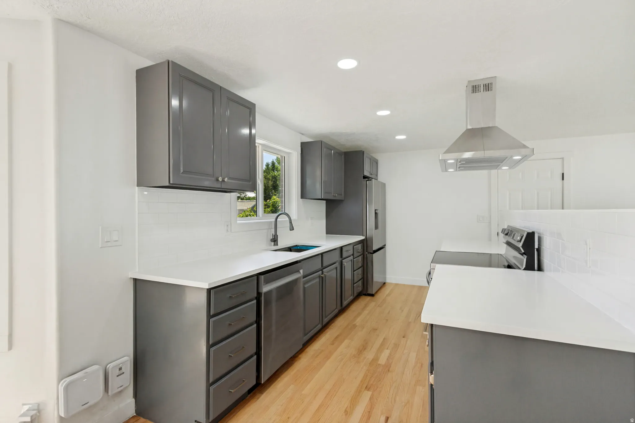 Modern kitchen featuring gray cabinetry, white countertops, stainless steel appliances, a white tile backsplash, and light wood-finish flooring