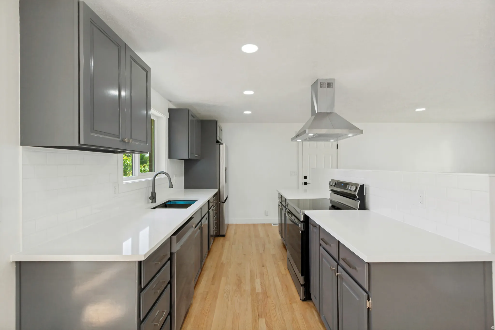 Kitchen featuring sleek gray cabinetry, white countertops, stainless steel appliances, a subway tile backsplash, and wood-finish flooring