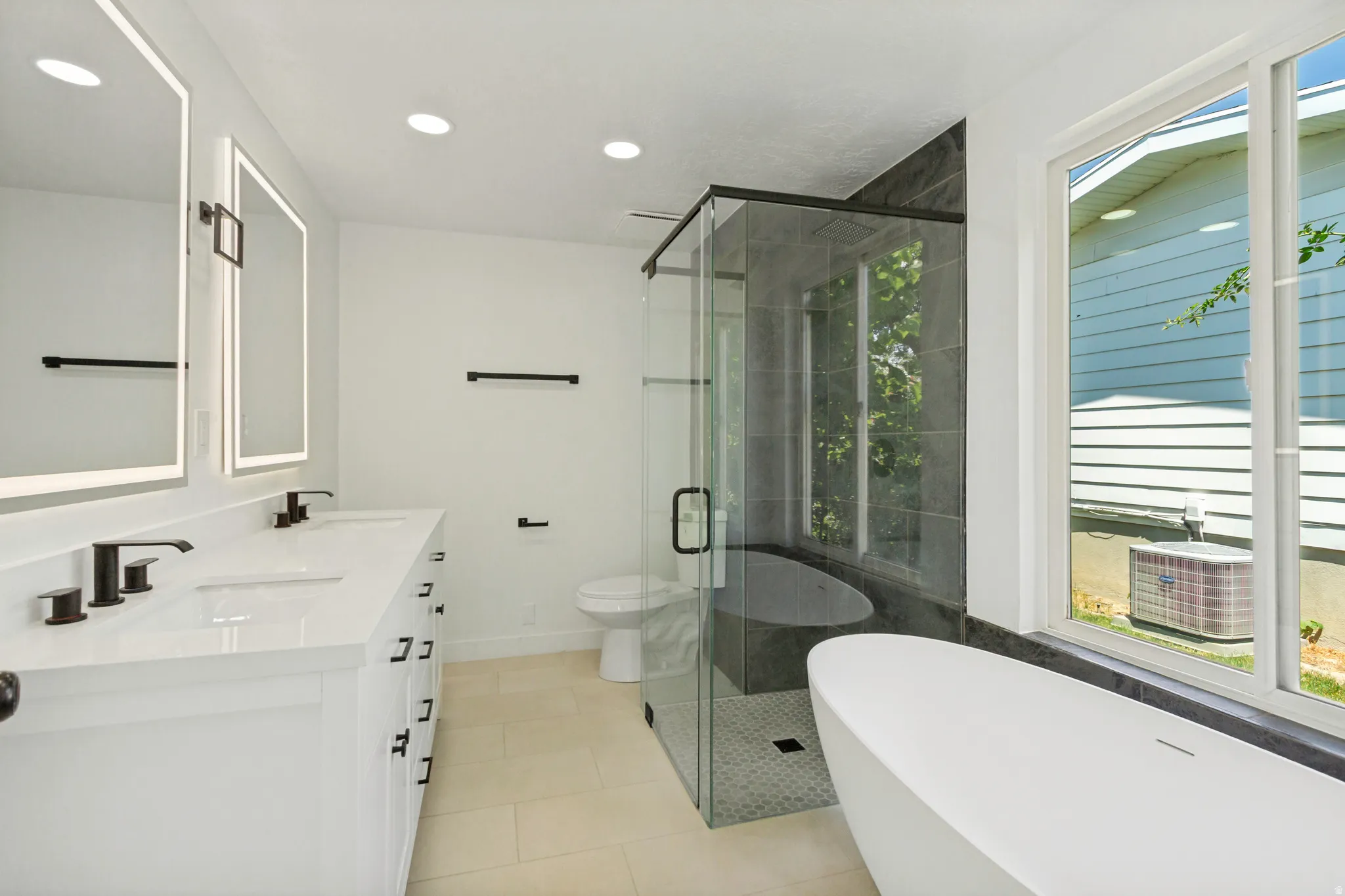 Spa-inspired bathroom featuring a freestanding soaking tub, frameless glass shower enclosure with dark tile surround, and a dual vanity with integrated sinks