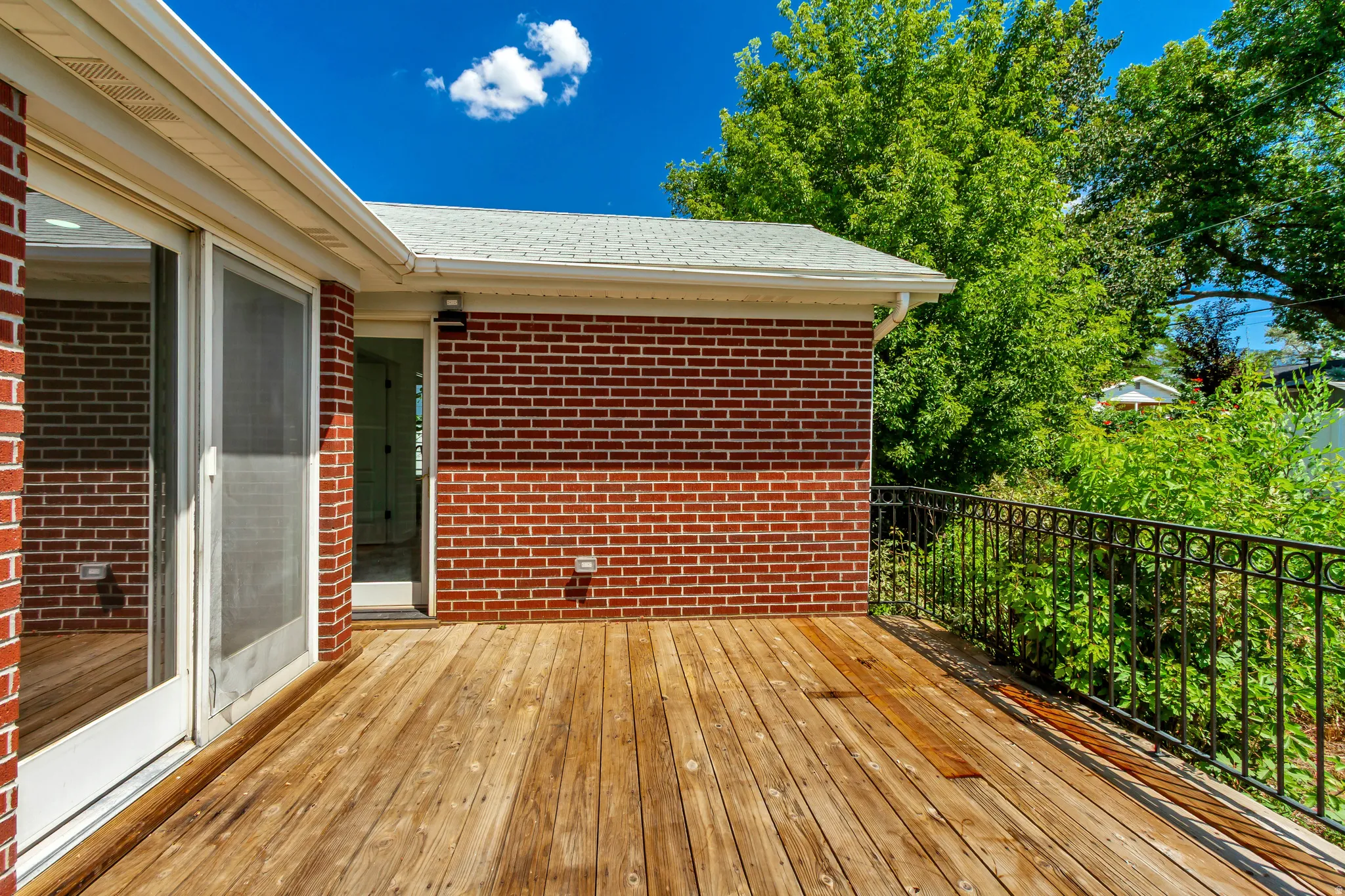 Wood-finish deck with a black metal railing, offering direct access to the interior via a sliding glass door and a standard entry door