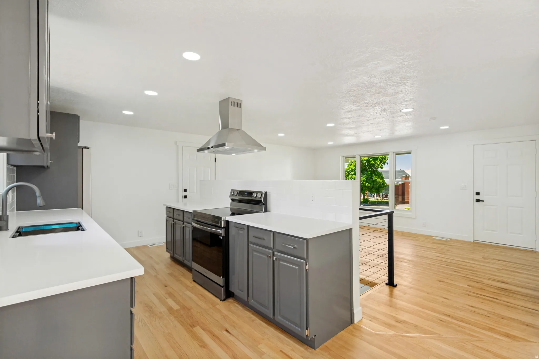 Modern kitchen featuring light wood-finish flooring, recessed lighting, white countertops, gray cabinetry, and a stainless steel range hood