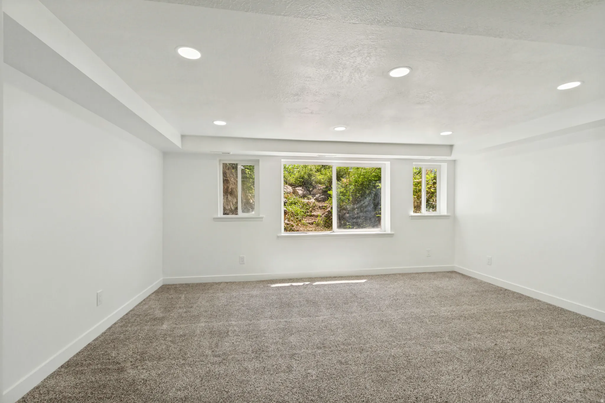 Spacious room featuring neutral carpeting, white walls, recessed lighting, and multiple windows