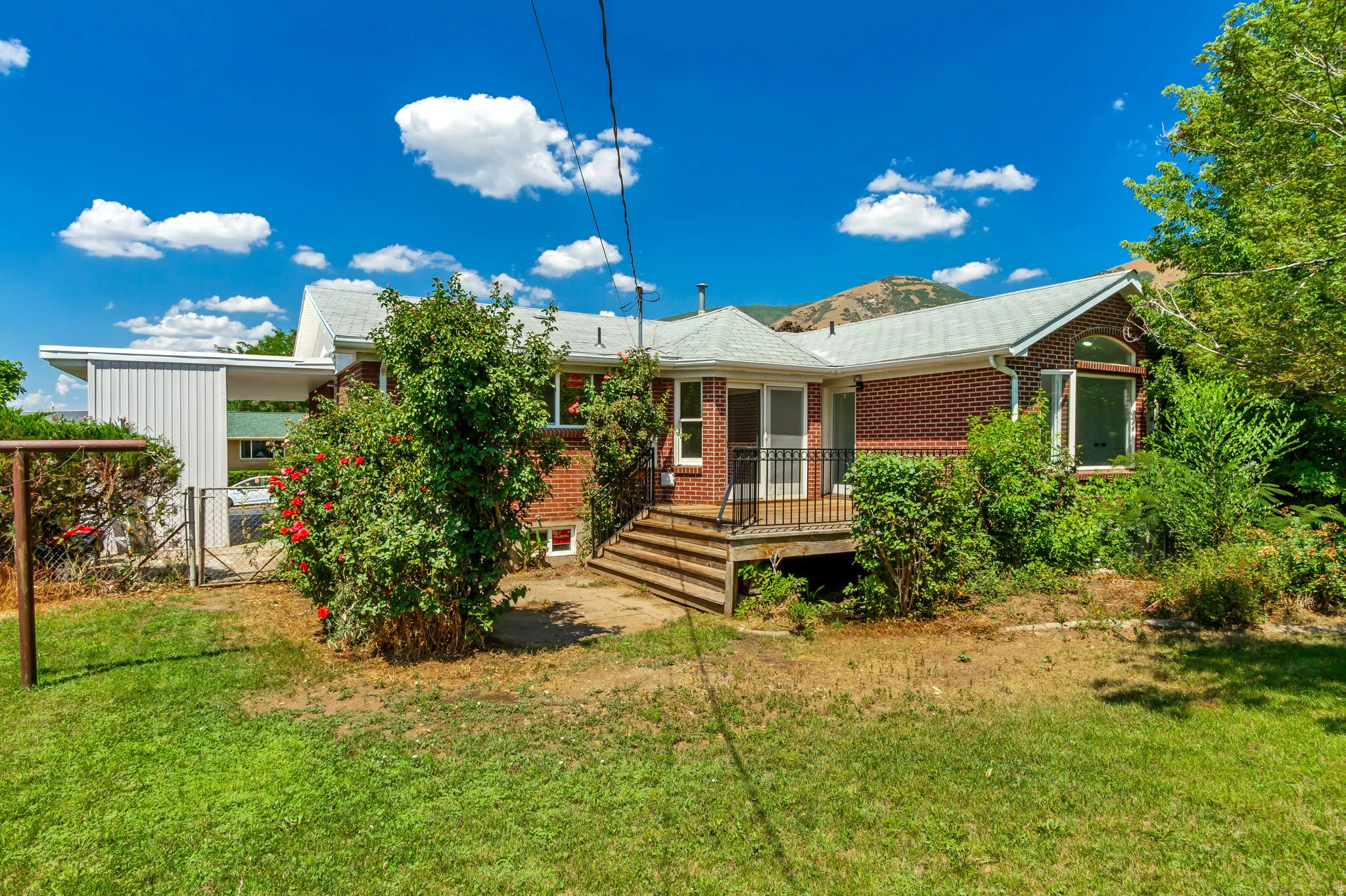 Red brick exterior with a rear wooden deck, bay window, and covered carport
