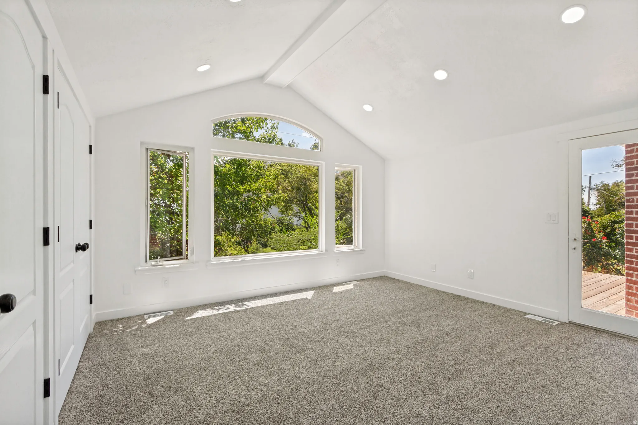 Vaulted ceiling interior space featuring a large arched window, additional vertical windows, a glass-paneled door, and recessed lighting