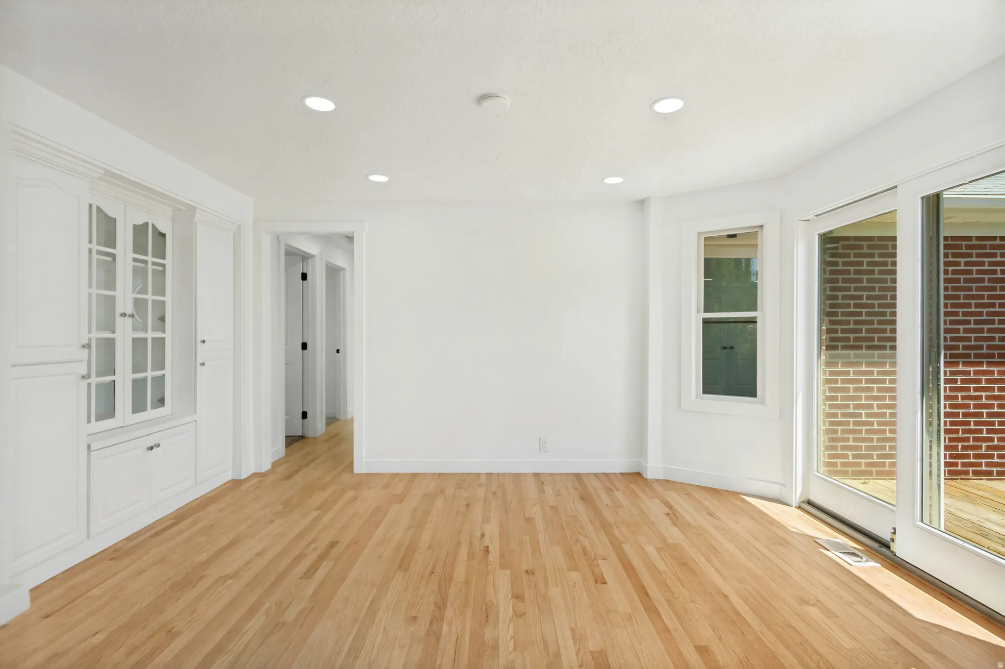 Room with wood flooring featuring white walls, recessed lighting, built-in cabinetry with glass-front display, and sliding glass doors