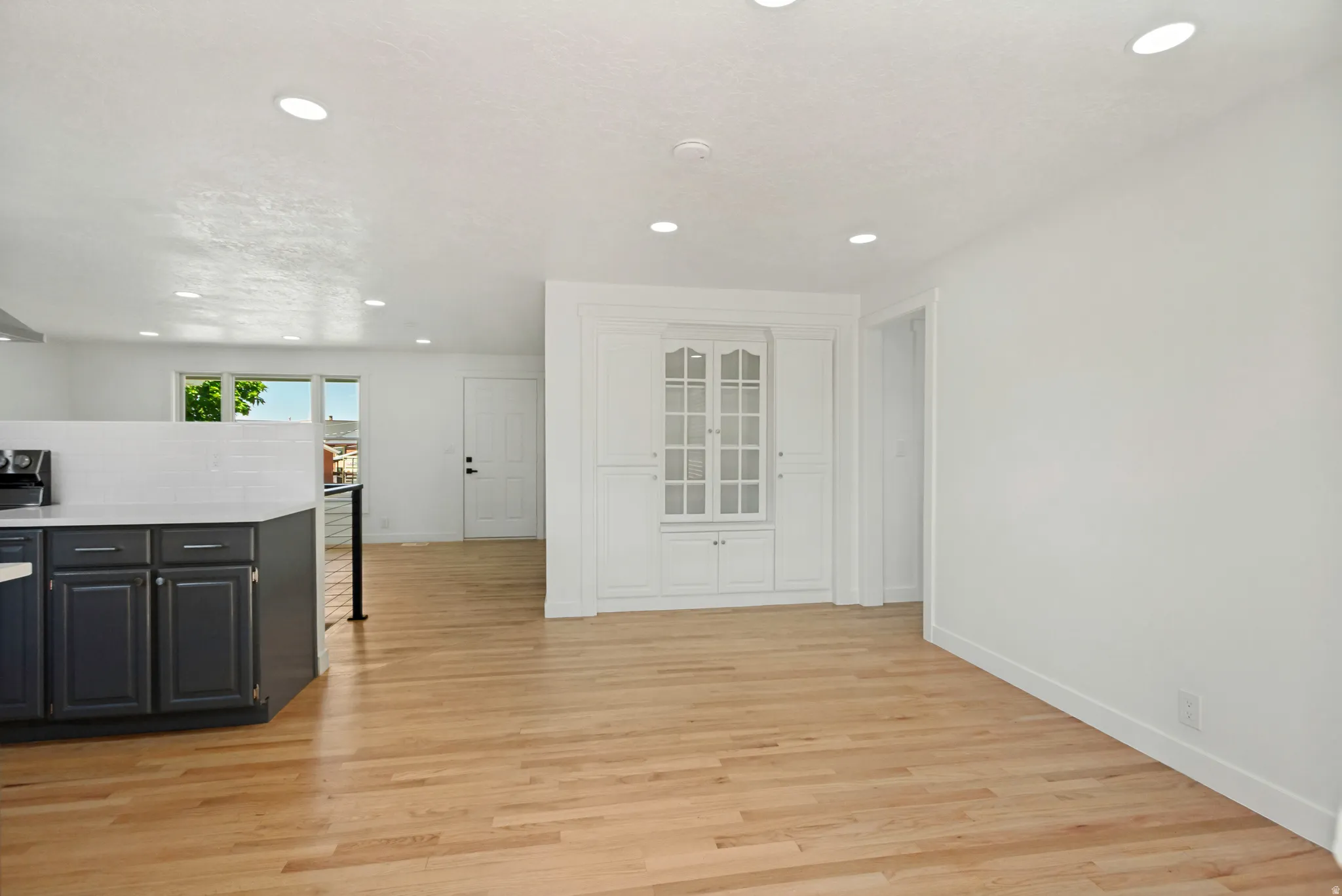 Open concept living area featuring wood-finish flooring, recessed lighting, and a built-in display cabinet with glass doors