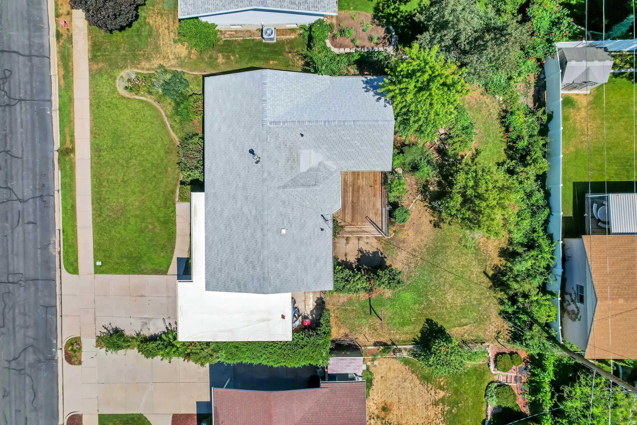 Aerial property showcasing a light gray shingle roof, a rear wood deck, a concrete driveway, and a manicured front lawn