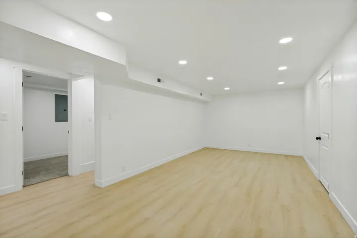 Spacious room featuring light wood-finish flooring, recessed ceiling lighting, white walls, and white baseboards