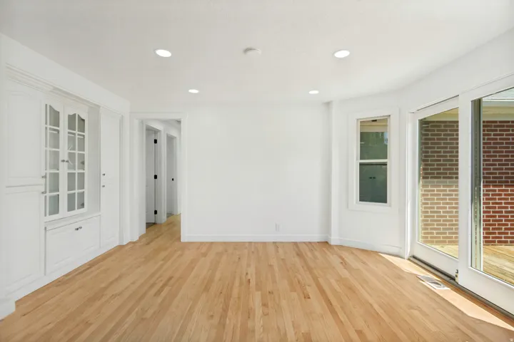 Room with wood flooring featuring white walls, recessed lighting, built-in cabinetry with glass-front display, and sliding glass doors
