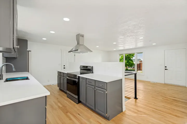 Modern kitchen featuring light wood-finish flooring, recessed lighting, white countertops, gray cabinetry, and a stainless steel range hood