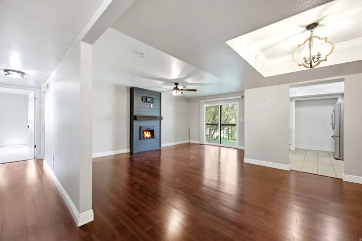 Spacious living area featuring rich wood-finish flooring, a contemporary fireplace with mantel, a ceiling fan, and sliding glass doors opening to outdoor space