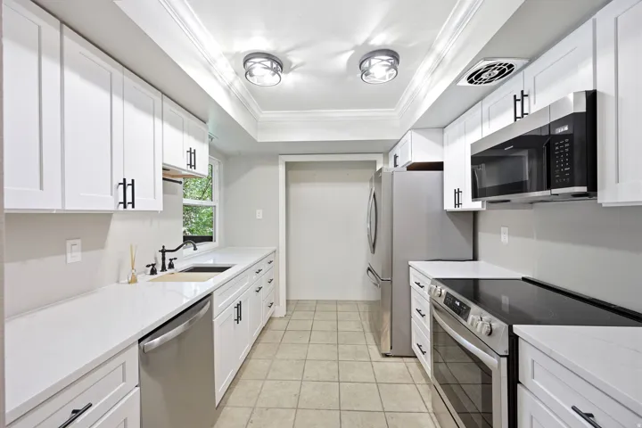 Galley kitchen featuring white cabinetry, stainless steel appliances, white countertops, and tile flooring.