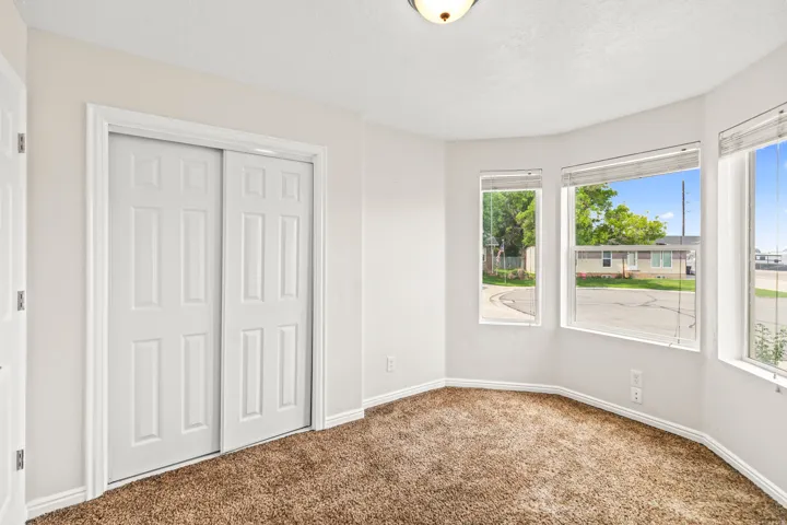 Room featuring a bay window with multiple panes, neutral wall paint, white trim, and brown textured carpeting