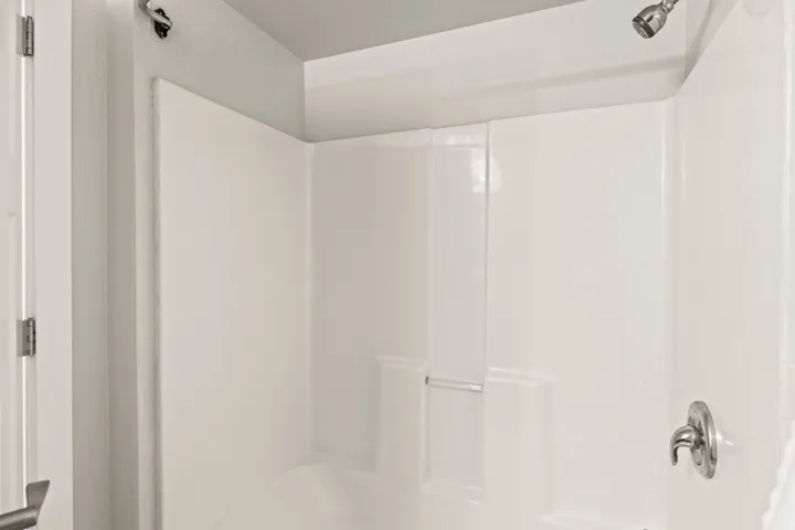 White shower and tub combination with built-in shelving, a chrome shower head, and a chrome single-handle faucet
