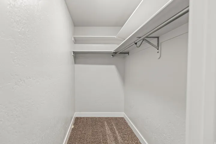 Walk-in closet with textured white walls, multiple shelving units, and clothing rods