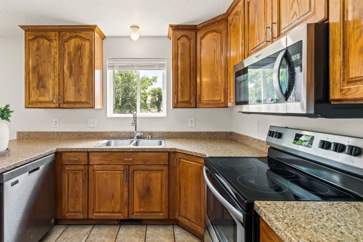 Kitchen featuring wood cabinetry, solid surface countertops, stainless steel appliances, a double basin sink, and tile flooring
