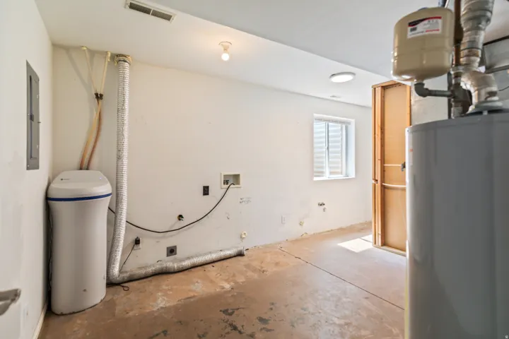 Utility space featuring a water softener system, water heater, and a basement window