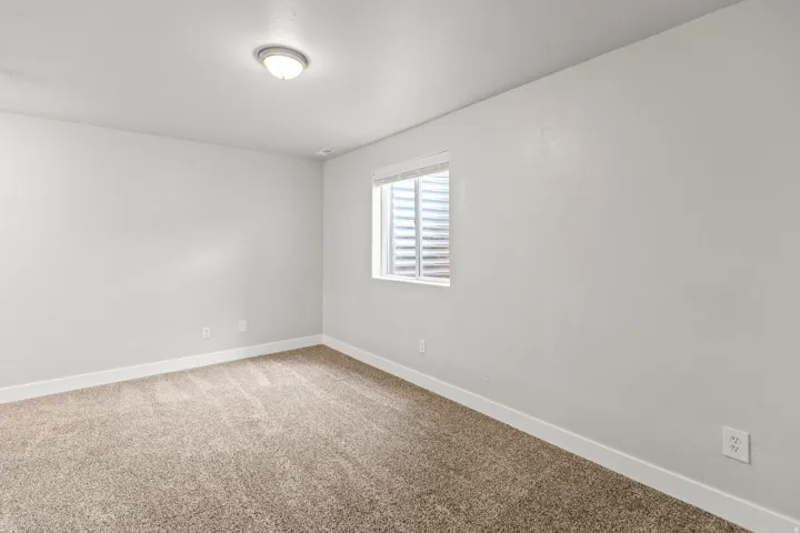 Carpeted room with a flush-mount ceiling light fixture, a window with horizontal blinds, and white baseboards