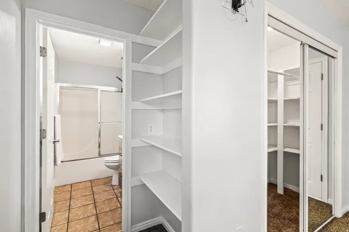 Hallway featuring built-in shelving, a full bathroom with a tub/shower combination, and a mirrored sliding closet door revealing additional shelving
