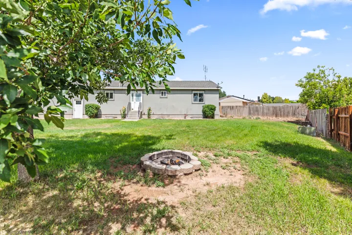 Expansive backyard with a stone-lined fire pit, mature perimeter fencing, and a stucco exterior