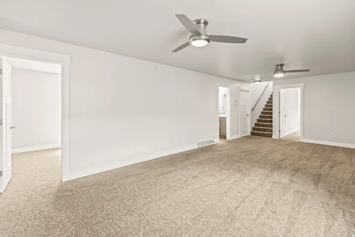 Expansive carpeted room featuring two brushed nickel ceiling fans, white baseboards, and a neutral wall color