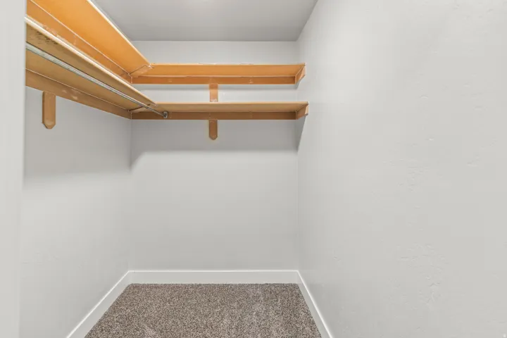 Walk-in closet featuring light wood shelving, a metal hanging rod, light gray walls, and gray carpet flooring with white baseboards