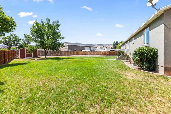 Expansive lawn area featuring a wooden privacy fence, mature trees, and a detached storage shed