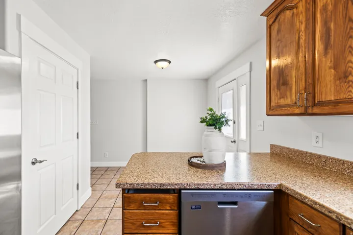 Kitchen with a built-in stainless steel dishwasher, wood-finish cabinetry, and speckled countertops