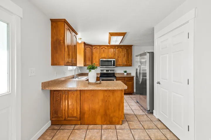 Kitchen featuring wood cabinetry, stone-finish countertops, stainless steel appliances, and tile flooring