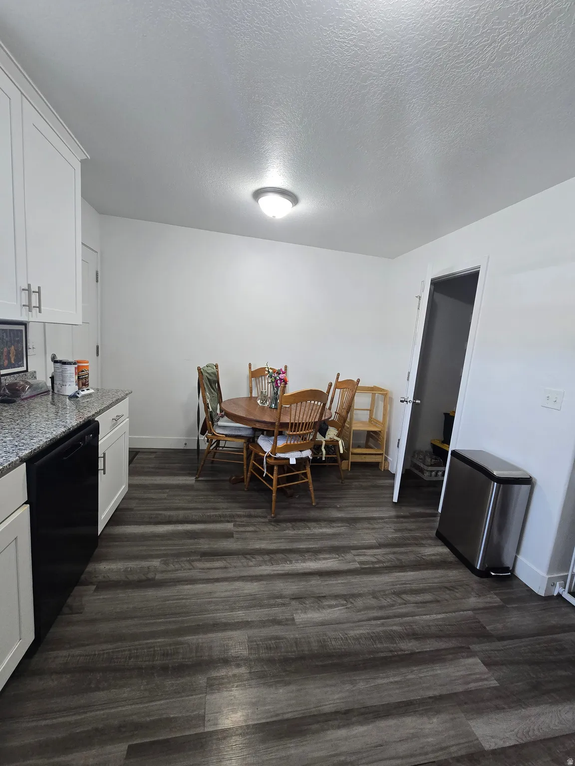 Kitchen area featuring wood-finish flooring, white cabinetry, a black dishwasher, and granite-style countertops