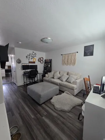Spacious living area featuring wood-finish flooring, a wall-mounted television, and a ceiling-mounted light fixture