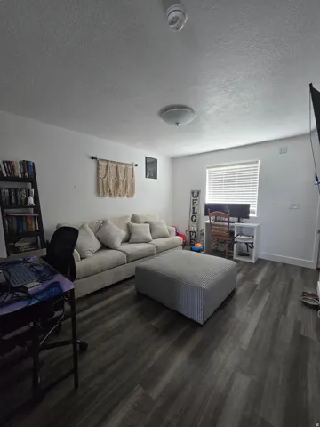 Living area featuring dark wood-finish flooring, white walls, and a recessed window with blinds