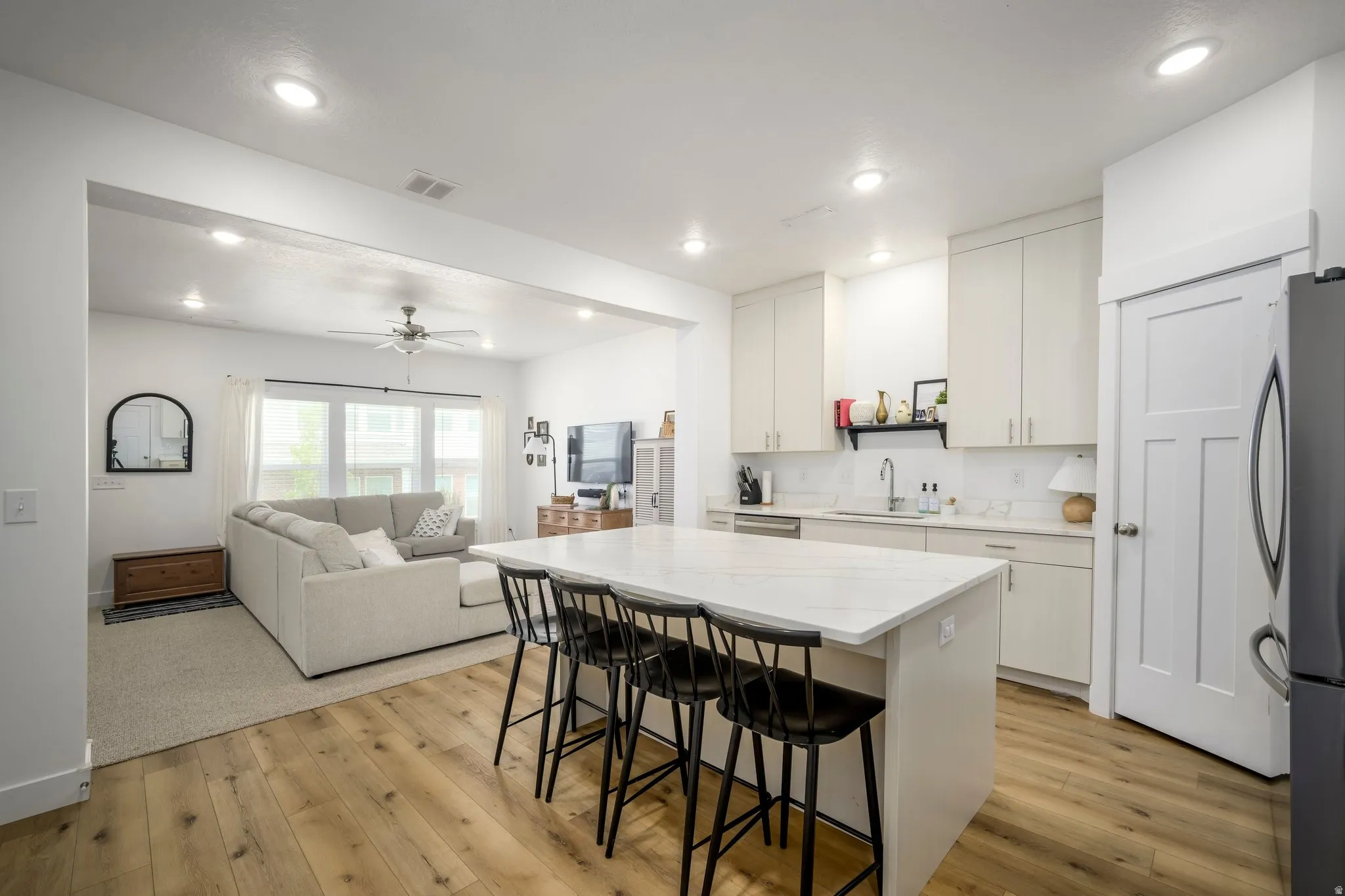 Modern kitchen featuring a white quartz-finish island with seating, light wood-finish flooring, white shaker-style cabinetry, and a white subway tile backsplash