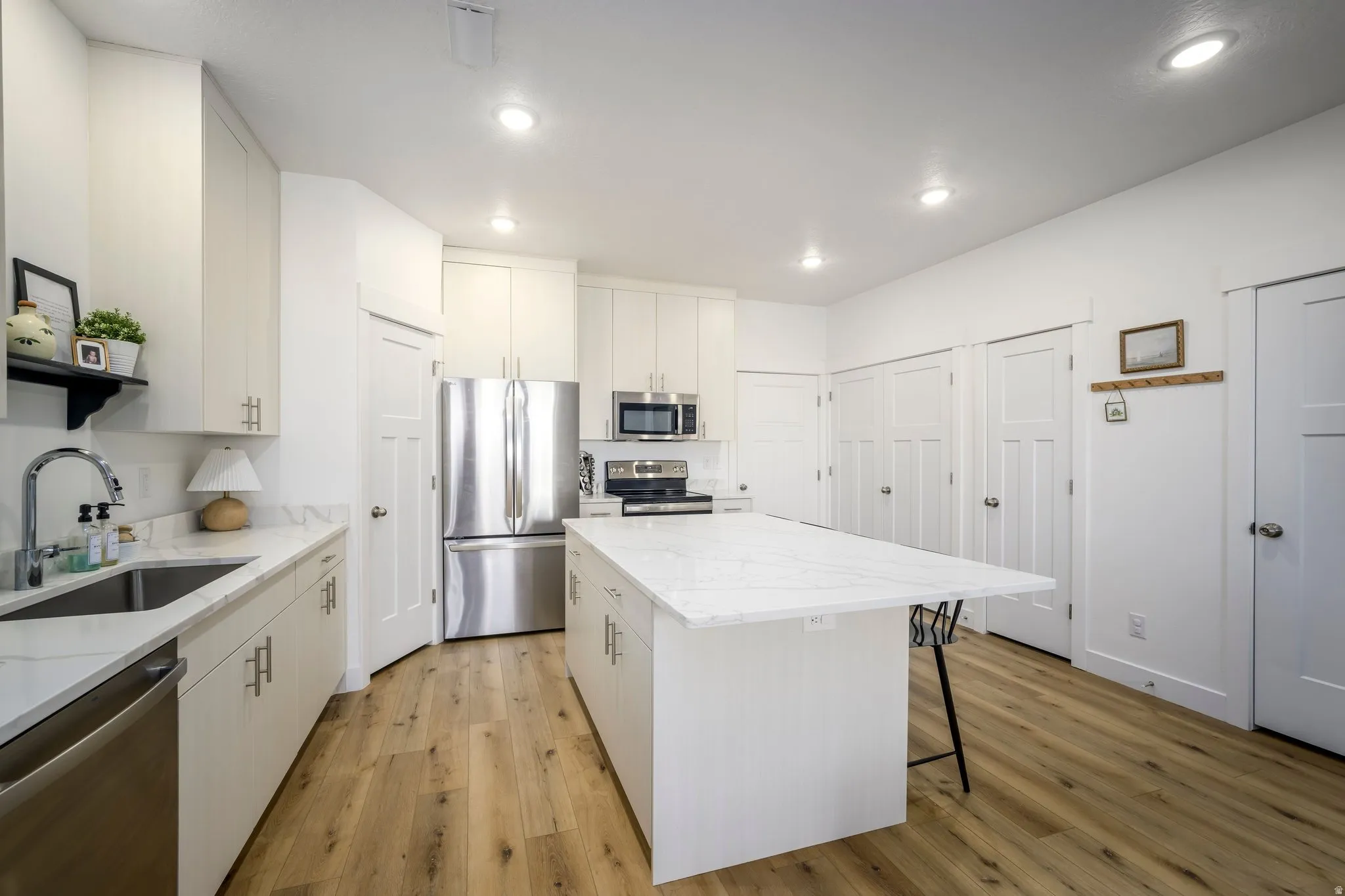 Modern kitchen featuring a large center island with a white countertop, recessed lighting, wood-finish flooring, white cabinetry, and stainless steel appliances
