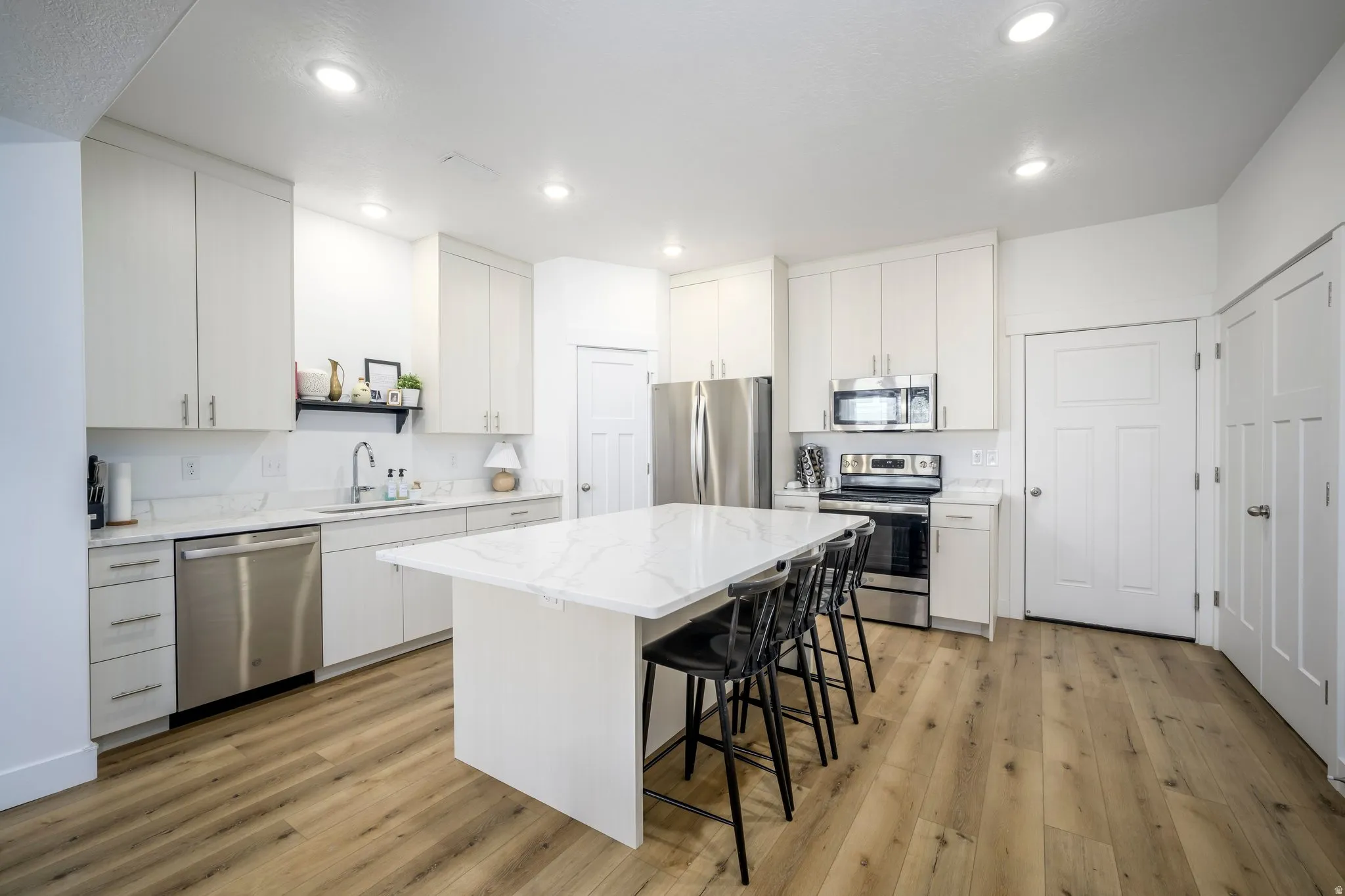 Modern kitchen featuring a large center island with seating, stainless steel appliances, white cabinetry, wood-finish flooring, and recessed lighting
