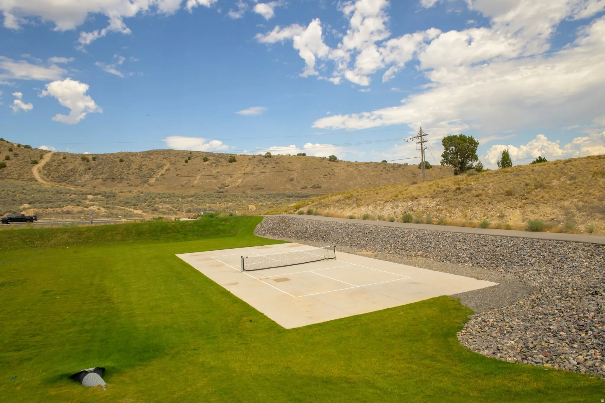 Outdoor concrete sports court with a net, bordered by manicured lawn and a gravel rock bed