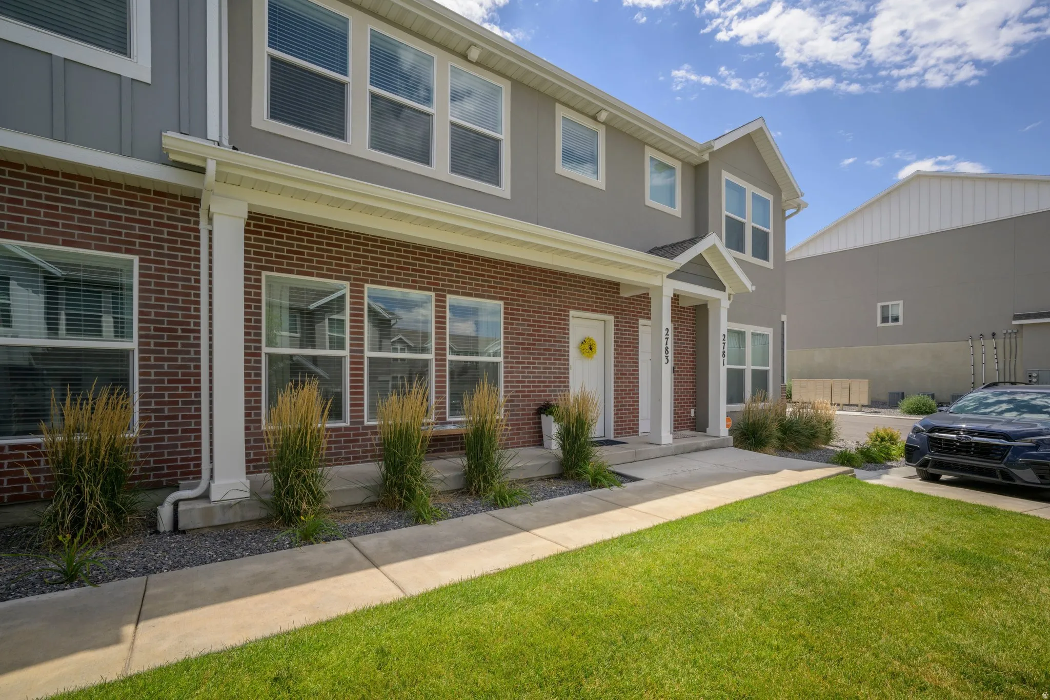 Exterior featuring brick and gray siding, multiple windows with white frames, a covered entryway, a front lawn, and a concrete pathway