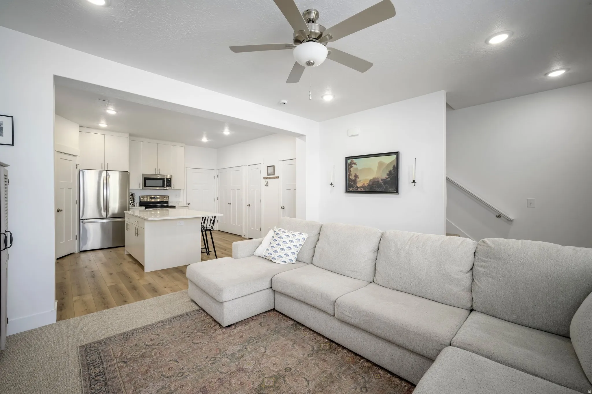 Open-concept living area featuring a kitchen with white cabinetry and stainless steel appliances