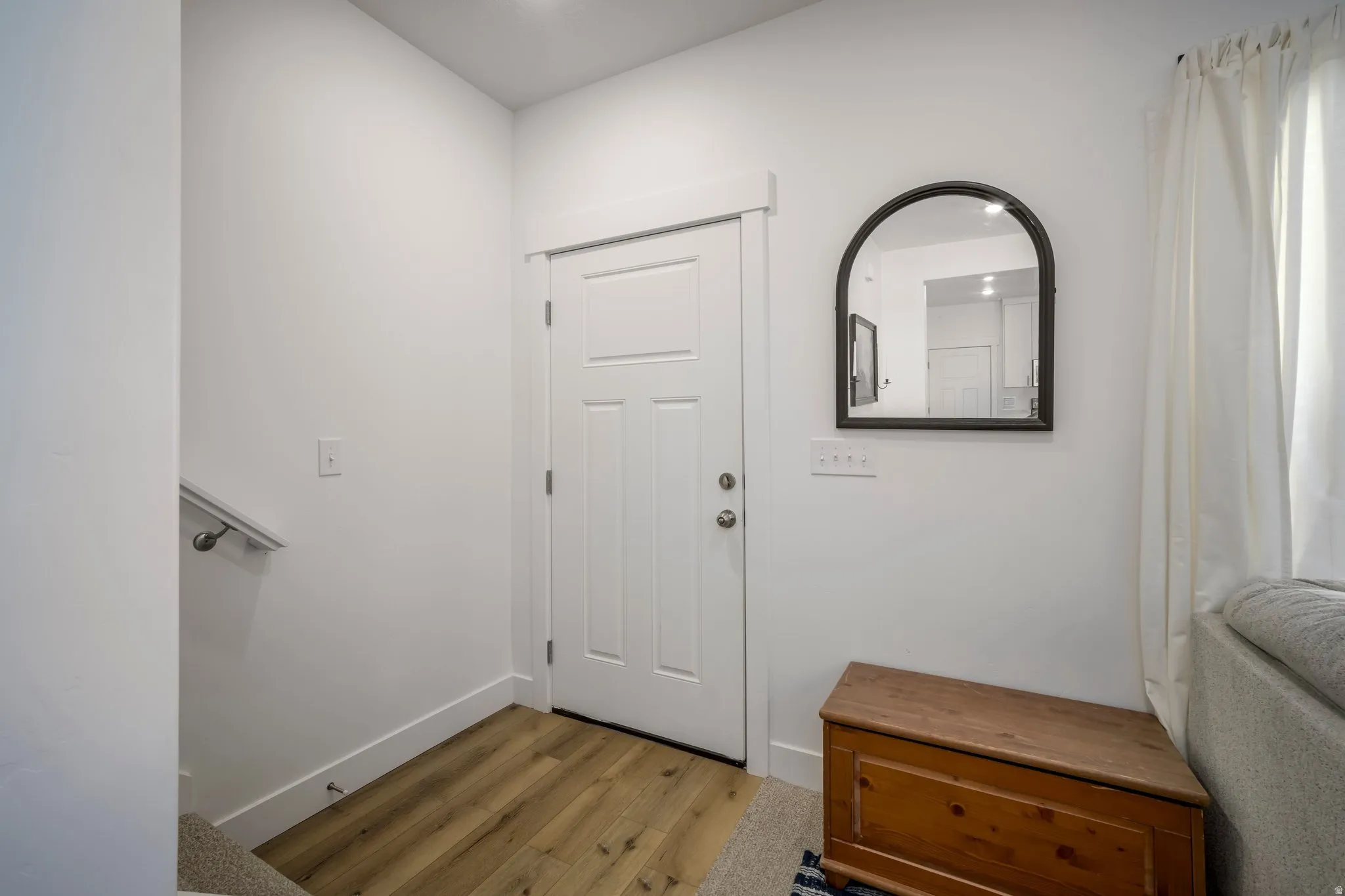 Entryway featuring light wood-finish flooring, white walls, and a white paneled door with brushed nickel hardware
