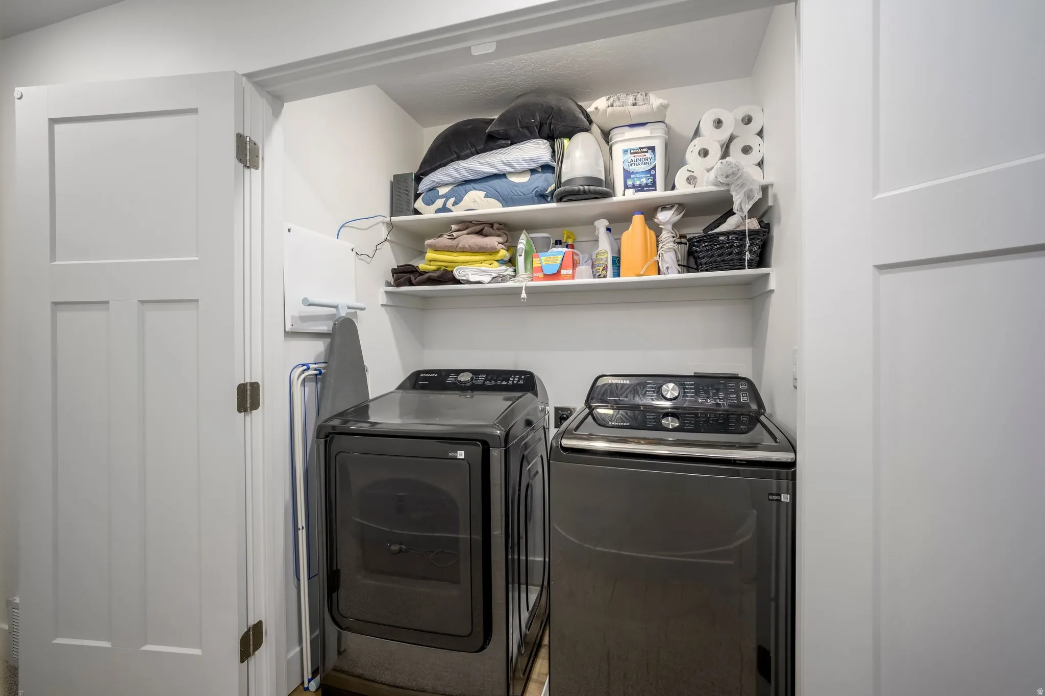 Recessed laundry area featuring built-in shelving, white paneled doors, and ample overhead storage