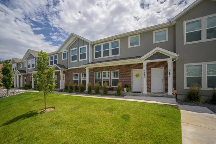 Contemporary townhome exterior featuring a combination of brick and siding, multiple large windows, a covered front entry, and a manicured lawn