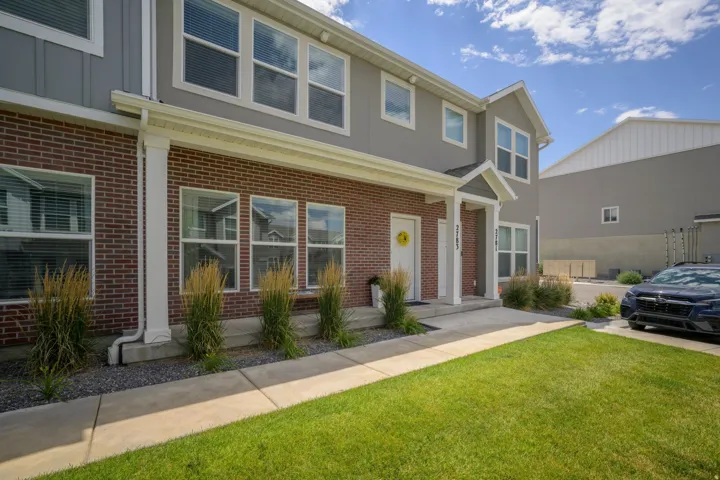 Exterior featuring brick and gray siding, multiple windows with white frames, a covered entryway, a front lawn, and a concrete pathway