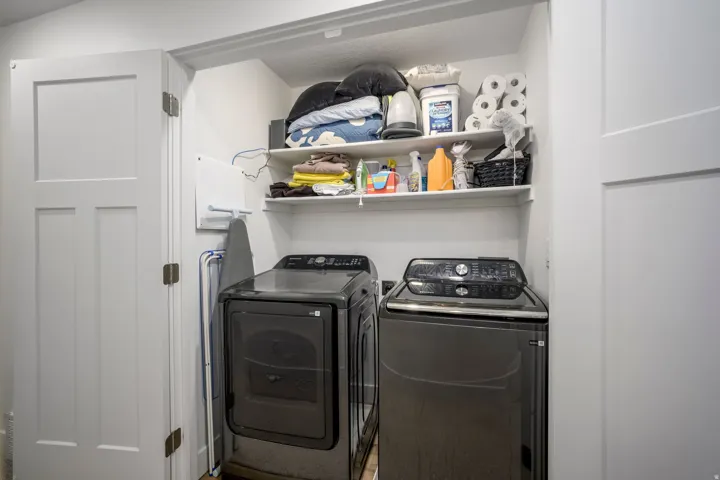 Recessed laundry area featuring built-in shelving, white paneled doors, and ample overhead storage