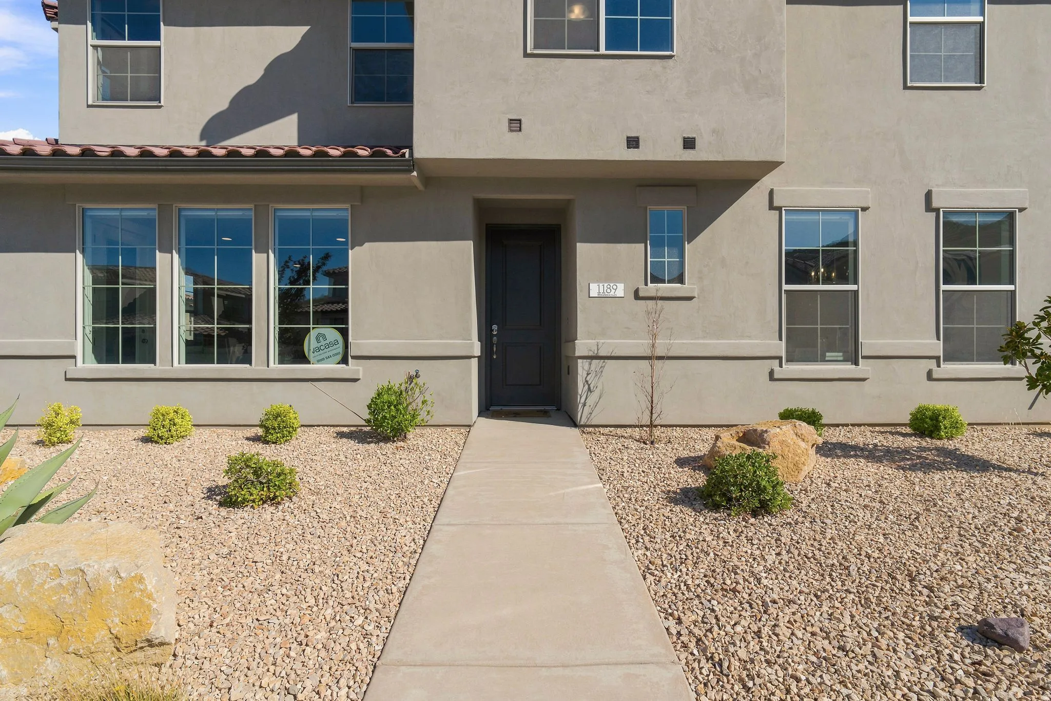 Contemporary stucco exterior with multiple windows, a prominent dark entry door, and a concrete pathway