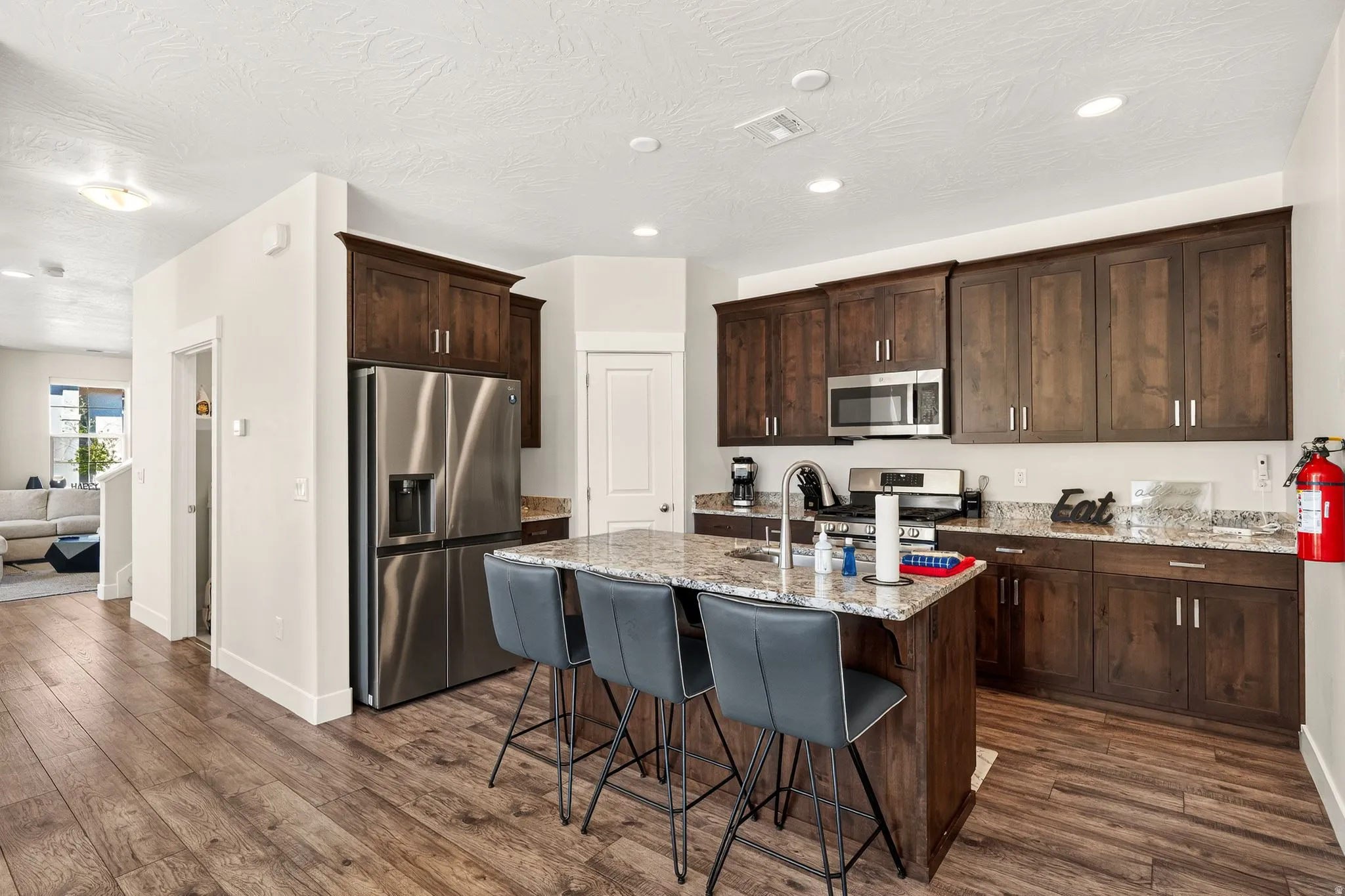 Modern kitchen featuring wood-finish flooring, dark wood cabinetry, stainless steel appliances, a center island with bar seating, and granite countertops
