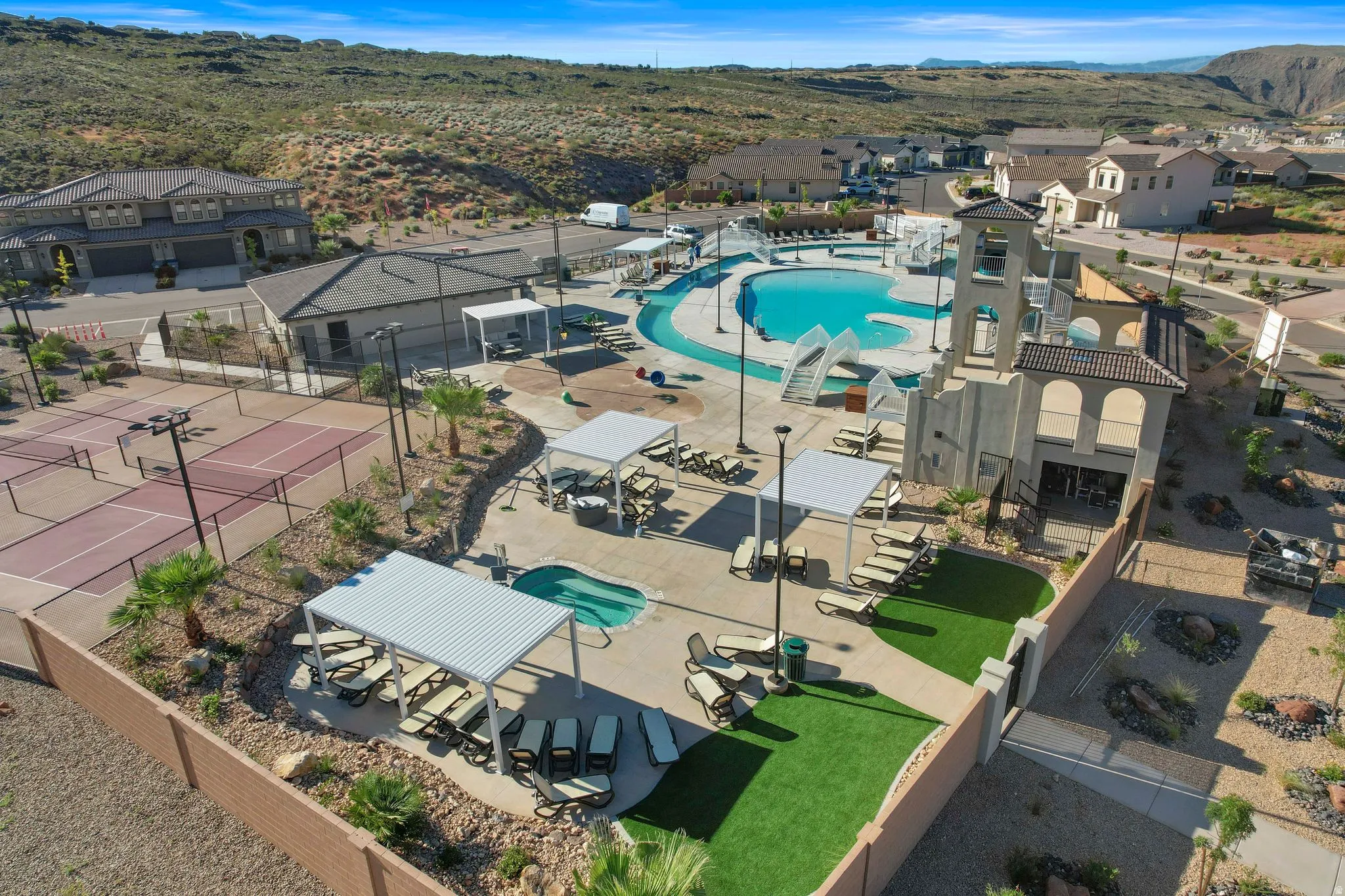 Community recreation area featuring a large swimming pool with water slides, a spa, shaded lounge areas, and multiple tennis courts