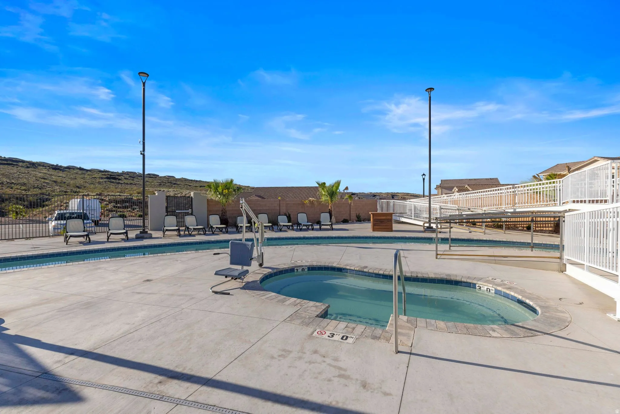 Concrete pool deck featuring an in-ground spa with a handrail, a rectangular swimming pool, and dedicated lounge areas